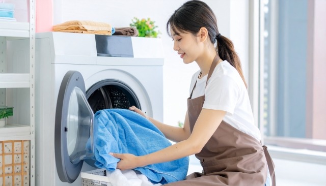 座って、ドラム式洗濯乾燥機から洗濯物を出し入れしている女性の写真