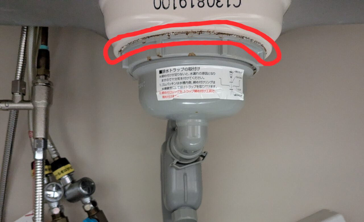 水漏れ修理前のシンク下、排水トラップの写真。水漏れ部分に赤丸をつけている。